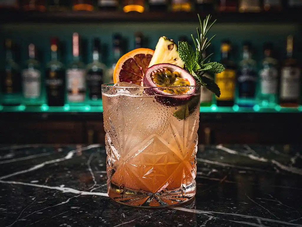 Berijpte cocktailglas met exotisch fruit en verse kruiden op donker marmeren bar, rijen premium spirits op de achtergrond.